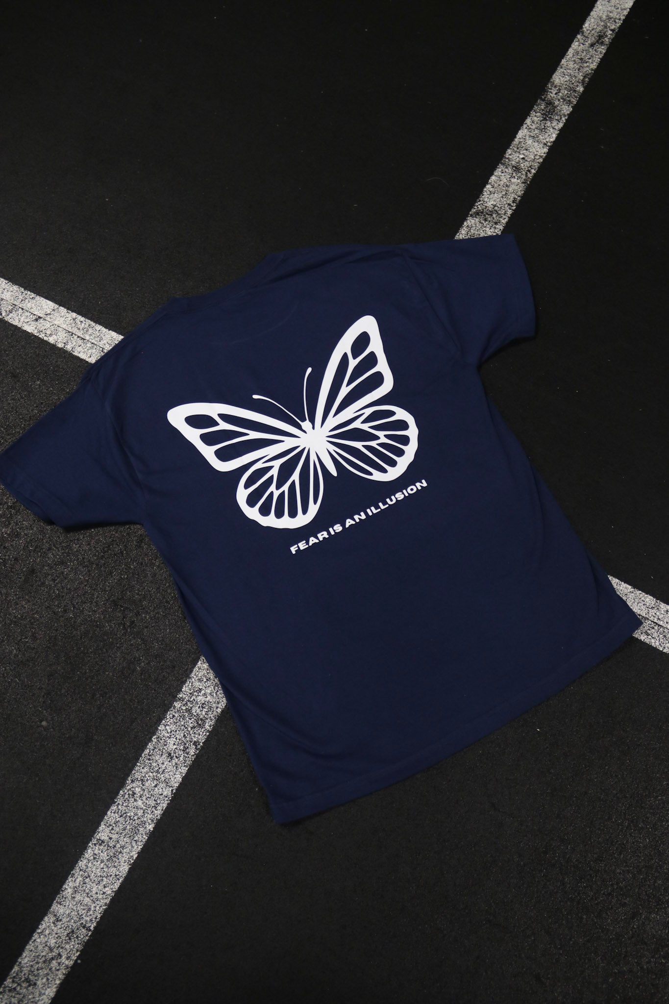 Navy blue t-shirt with a white butterfly design and text on a dark surface.